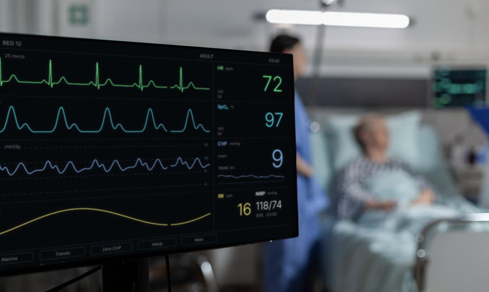 A patient monitor showing a central venous pressure reading, with a patient resting in a hospital bed behind it
